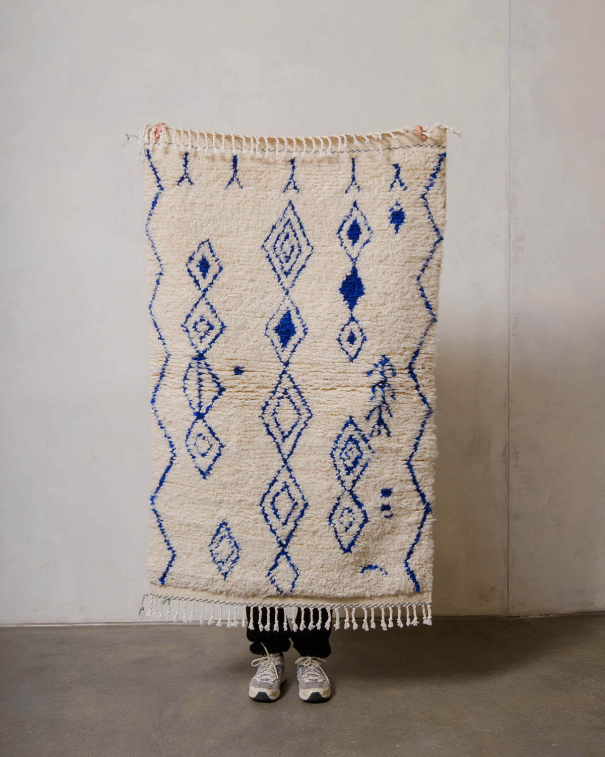 Berberlin Azilal rug in cream wool with blue cotton being held up in front of a white wall.